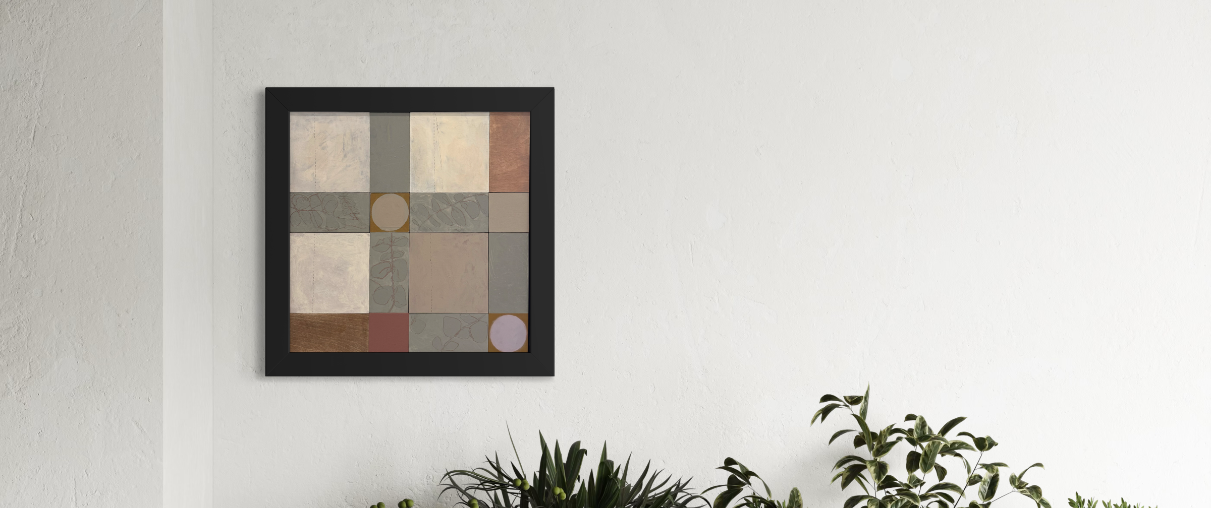 Framed geometric art piece on a white wall with green plants at the bottom.